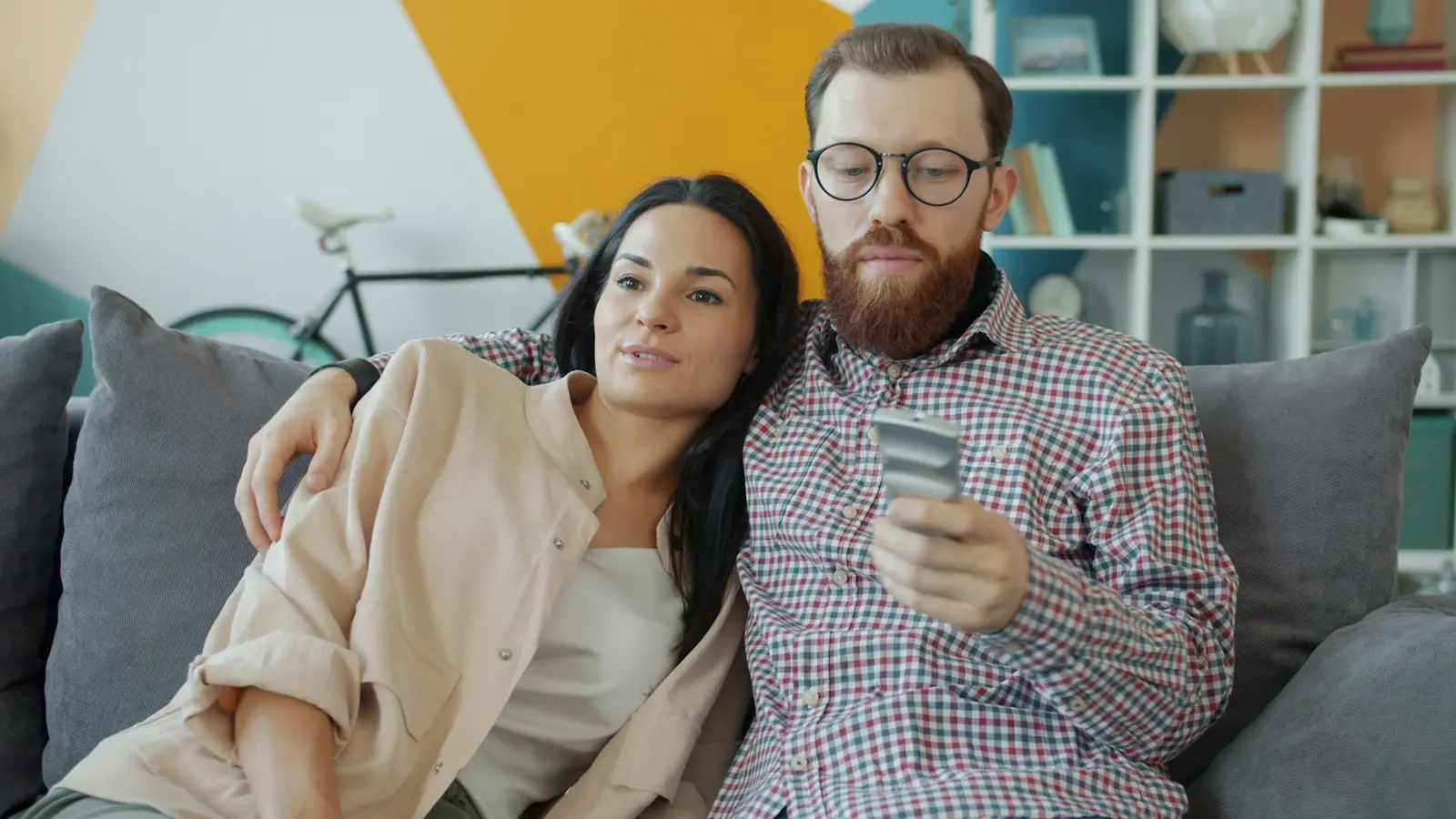 Couple on a sofa comparing TV subscription costs with a card in hand